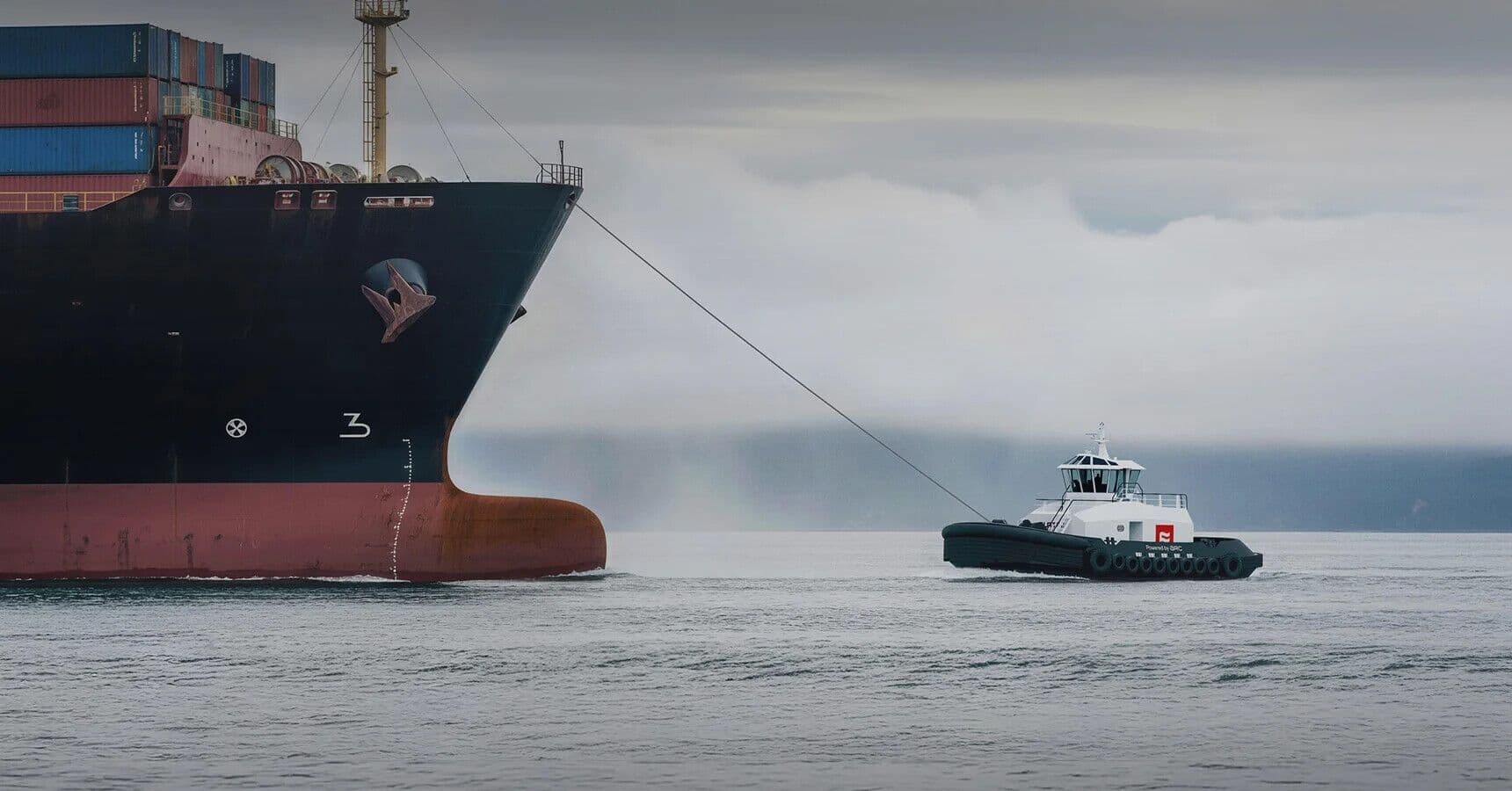 A photograph of a tug boat on a line with a freight ship.