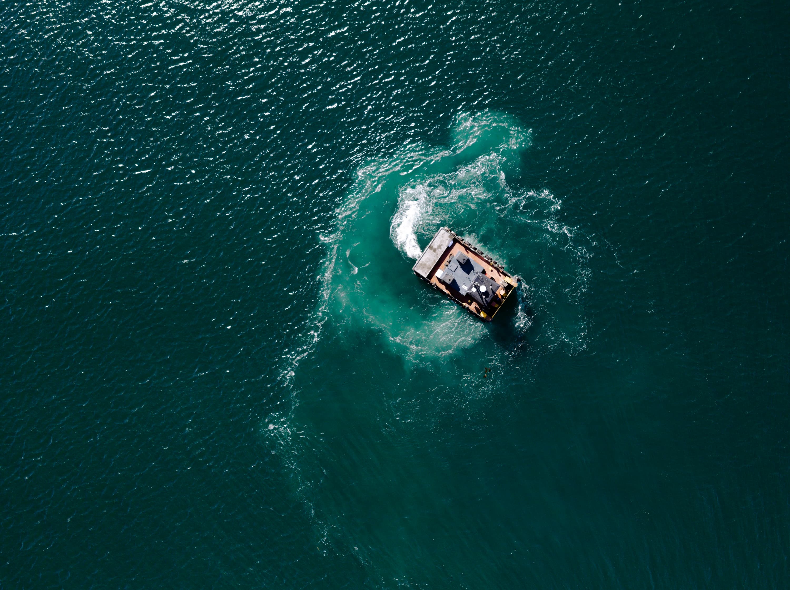 An aerial photograph of a work boat turning in the water.