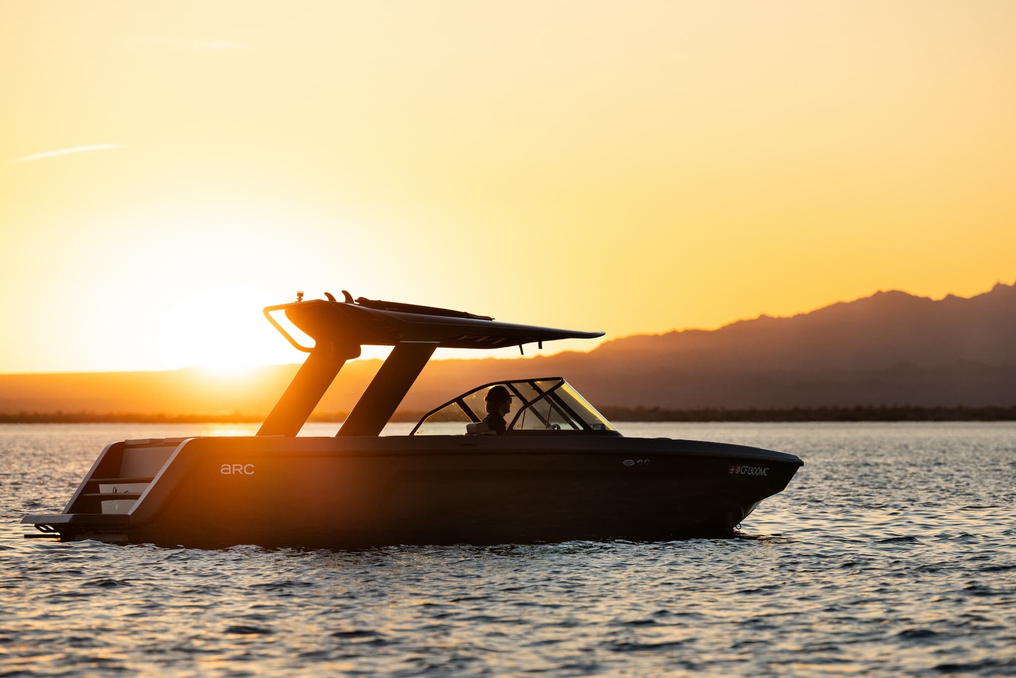 A photograph of a silhouette of a sporty boat floating on the water in front of an orange sunset.